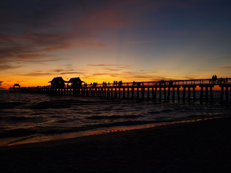 people walking a pier over the gulf colorful sunset
